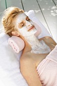 A blonde woman relaxing with a nourishing mask on her face, neck and chest