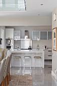 Modern kitchen in shades of grey, plexiglas bar stools at island counter and dining chairs in foreground