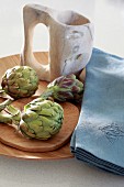 Artichokes, blue linen napkins and jug on wooden dish