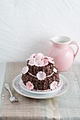 A chocolate cake decorated with chocolate butter cream ruffles with cherry jam and sugar cherry blossom
