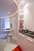 View from kitchenette into circular living area with suspended ceiling panel above table and Ghost chair