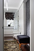 Antique ottoman with black velvet cover and rug on tiled floor in comfortable bathroom with modern ambiance