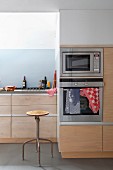 Vintage bar stool in subdued fitted kitchen with wooden fronts, polished concrete floor and pale blue splashback