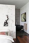 Subtle floral wallpaper on partition with ethnic sculpture on shelf and view of free-standing bathtub in ensuite bathroom