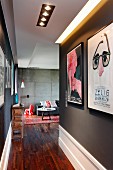 Narrow hallway with posters on black wall and view into lounge area with concrete wall