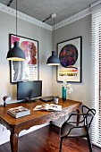Modern black plastic chair at antique table below pendant lamps in corner of room with pale grey walls and white stucco frieze