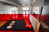 Schlafbereich auf Galerie, Doppelbett mit schwarzer Tagesdecke und roten Kissen vor roter Glasbrüstung