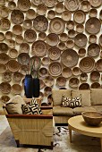 Collection of many wooden bowls on wall behind wicker sofa set with ecru upholstery and geometric scatter cushions