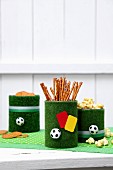 Snack in old tin cans covered with artificial grass decorated with mini footballs and yellow and red referees' cards
