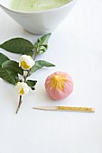 Wagashi plum (ume) next to a flowering sprig of tea leaves and a bowl of matcha tea