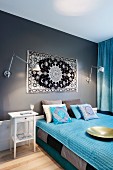 Grauweisses Interieur eines Schlafzimmers mit himmelblauen Wohntextilien und Folklore-Akzenten