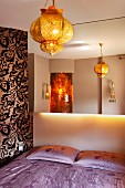 Mirrored wall above double bed with lilac bed linen, gold oriental pendant lamp and floral wallpaper on accent wall