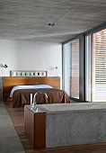 Concrete bathtub and double bed with brown bedspread in bedroom with concrete ceiling