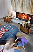 Detail of living room - children playing on floor in front of large, denim beanbag, crate of firewood on castors and fire in fireplace