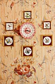 Sammlung von gerahmten Vogelbildern an tapezierter Wand mit Blumenmotiv, in der Mitte rotweiss gemusterter Uhr-Wandteller