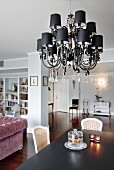 Chandelier with small black lampshades and glass pendants above dining table in open-plan interior with walls painted pale grey