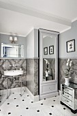 Mirrored cupboard in niche next to retro washstand with metal frame in traditional bathroom with walls tiled below dado rail and painted pale grey above
