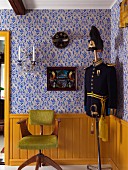 Wooden swivel chair with lime green fur cover and tailors' dummy wearing old uniform against yellow-painted wainscoting below ornamental blue wallpaper