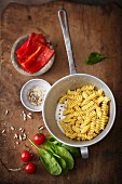 Cooked fusilli in a colander with ingredients for pepper sauce