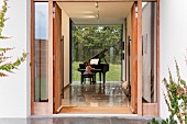 Blick durch offene Eingangstür in Foyer eines Wohnhauses, Mädchen an Klavierflügel mit Verglasung zum Garten