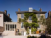 Traditional house with climber-covered brick facade, terrace and steps leading to extension on one side