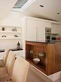Upholstered dining chairs in front of solid wood kitchen counter an white fitted cupboards in open-plan kitchen