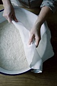 A woman covering a bowl of dough with a white cloth