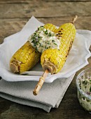 Corn cobs with herb butter on a white plate on a wooden table