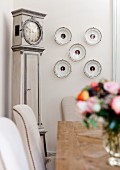 View across table to decorative wall plates next to antique long-case clock
