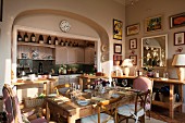 In Nische integrierte Küchenschränke und Wände in pastellrosa, vorne gepolsterte Armlehnstühle, Camargue Stühle und gedeckter Tisch aus alter Eiche