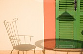 Schattenwurf von Stuhl und Tisch auf Hausfassade neben grünen Lamellentür