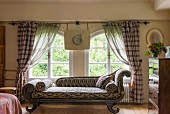 Antique chaise longue with ikat upholstery in front of arched windows with gathered curtains