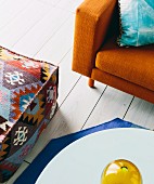 Orange-colored retro sofa, ethnic pouf and coffee table on white plank floor