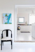 Black armchair next to an open door and a view of a white kitchen