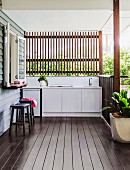 Slatted wall above outdoor kitchen on roofed wooden terrace