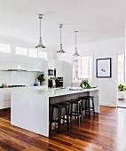 Stools at kitchen counter below retro pendant lamps in open-plan kitchen with white fronts and parquet floor