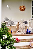 White mesh armchairs with cushions on narrow terrace with wooden steps and spherical rattan pendant lamp