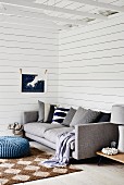 Modern grey sofa with row of scatter cushions, sisal rug on wooden floor in corner of room with white wooden cladding