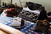 Vintage Schreibmaschine, Sonnenbrille und Notizbuch auf Holztisch mit Folklore-Decke