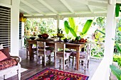 Esstisch mit einfachen Holzstühlen und Obstschalen auf Holzterrasse in tropischer Umgebung
