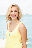 A blonde woman by the sea wearing a sleeveless, pastel yellow top