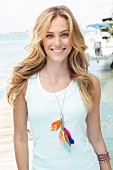 A blonde woman wearing a sleeveless top and a necklace with colourful feathers