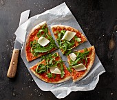 Pizza Margherita with rocket and Parmesan cheese on a piece of paper with a knife