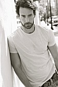 A young man wearing a light T-shirt leaning against the wall of a house (black-and-white shot)