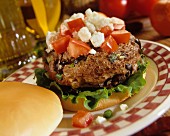 A Greek burger with black olives, chopped tomatoes and feta cheese