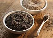 Chia seeds in bowls and on a spoon on a wooden surface