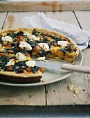 Chard quiche on a wooden board with a knife and a napkin