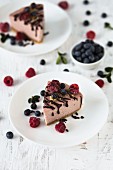 Two slices of raspberry cheesecake with fresh raspberries, blueberries and chocolate drizzle