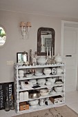Collection of crockery on white wooden shelves with carved uprights against wall