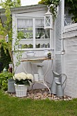 Vintage Waschschüssel und Krug in rostigem Metallgestell, weiße Hortensien im Zuber vor Gartenhäuschen